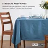 A table set with blue tablecloth, white plates, bowls, and glasses, next to a wooden chair. Text overlays describe stylish must-haves. Náhled obrázku produktu