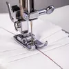 Close-up of a sewing machine needle and presser foot stitching white fabric with red thread. Produktbild-Vorschau
