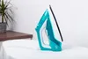 A teal and white iron stands on a white towel, next to a plant on a wooden table. Produktbild-Vorschau