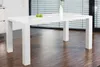 A white dining table with two green apples and a vase on it, placed in a room with wooden flooring and blinds in the background. Produktbild-Vorschau