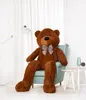 A large brown teddy bear sitting in a light blue armchair in a room with white curtains and a floor lamp. Podgląd zdjęcia produktu