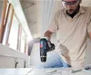 A person is using a cordless drill to drill into a tiled surface. Voir les images du produit