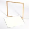 A wooden frame is placed diagonally over a white rectangular board, both on a white background. Produktbild-Vorschau