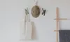 A wall with hooks holding a tote bag, a cap, and a decorative figure. A wooden ladder with a blanket is on the right. Náhled obrázku produktu
