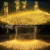 A net of warm white fairy lights is draped over garden decorations and a patio umbrella, creating a festive atmosphere. Náhled obrázku produktu