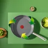 A frying pan with recycling arrows around it, placed on a green surface with a green bell pepper and a bowl of lettuce in the background. Podgląd zdjęcia produktu
