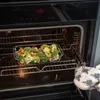 A glass baking dish filled with broccoli and red peppers is being removed from an oven by a person wearing an oven mitt. Anteprima dell’immagine prodotto