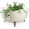 A cream-colored planter with three wooden legs, holding a green ivy plant. A product tag is attached to the planter. Voir les images du produit