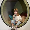 A young girl is sitting in a circular, cushioned nook, drinking from a water bottle. Produktbild-Vorschau