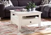 A white coffee table with a drawer and shelf is placed on a patterned rug in front of a dark gray sectional sofa. Produktbild-Vorschau