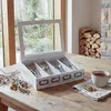 A wooden cutlery box with a glass lid sits on a wooden table next to a cup of tea and some dried herbs. Voir les images du produit