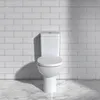 A white toilet against a white tiled wall and a marble-tiled floor. Anteprima dell’immagine prodotto