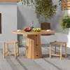 An outdoor patio scene with a round wooden table and two wooden stools, set with fruit and cups. Produktbild-Vorschau