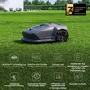 A robotic lawnmower is shown on a green lawn, with a modern house and garden in the background. Below the lawnmower are several icons and text describing its features. Produktbild-Vorschau