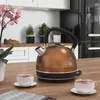 A copper kettle is shown on a wooden countertop next to two cups of tea, with kitchen cabinets and a refrigerator in the background. Anteprima dell’immagine prodotto