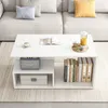 A white coffee table with storage shelves is placed in a living room setting, next to a sofa. The table holds decorative items and books. Produktbild-Vorschau