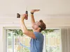 A man is drilling a hole in the ceiling while wearing safety glasses. Podgląd zdjęcia produktu