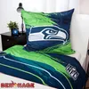 A bedding set with a Seattle Seahawks theme is displayed on a bed, with a nightstand and lamp in the background. Náhled obrázku produktu
