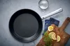 A frying pan is shown on a gray surface with lemons, dill, salt, and a blue napkin. Produktbild-Vorschau