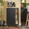 A black kitchen cart with a wooden top is shown in a kitchen setting. It has a coffee machine and a carafe on top, and a plant next to it. Produktbild-Vorschau