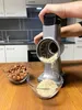 A person is using a rotary grater to grind nuts into a bowl in a kitchen setting. Produktbild-Vorschau