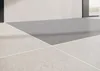 A close-up view of a modern shower tray with a gray surface and white tiled walls. Produktbild-Vorschau