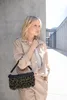 A woman stands next to a concrete wall, holding a handbag. Produktbild-Vorschau