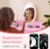 A young girl is applying makeup in front of a pink vanity mirror with LED lights. The image also includes marketing text and graphics highlighting the mirror's shatterproof feature. Náhľad obrázku produktu