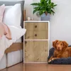 A dog is resting on a bed next to a nightstand with drawers, with a plant on top of the nightstand. Produktbild-Vorschau