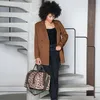 A woman stands on a spiral staircase holding a leopard-print duffel bag. Náhled obrázku produktu