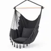 A dark gray hanging chair with tassels and cushions, suspended from a wooden bar.
