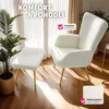 A white textured armchair and ottoman with gold legs are placed on a wooden floor near a window with sheer curtains. A potted palm plant is to the left. Náhled obrázku produktu
