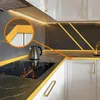 A close-up view of a modern kitchen countertop with a black marble pattern, featuring a gold trim accent. A silver kettle is placed on the countertop. Podgląd zdjęcia produktu