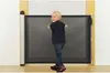 A young boy is standing in front of a retractable baby gate. Náhľad obrázku produktu