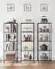 Three black metal shelving units are displayed against a white wall, each holding various items. Voir les images du produit