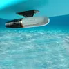 A white and black Aqua Marina BlueDrive X PRO Power Fin Tauchscooter und E-Motor is shown attached to the underside of a blue object, submerged in clear blue water with sunlight filtering through. Podgląd zdjęcia produktu
