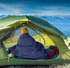 A person wrapped in a sleeping bag inside a tent, with a mountain landscape in the background. Produktbild-Vorschau