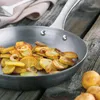 Fried potatoes and onions in a pan on a wooden table, with raw potatoes in the foreground. Voir les images du produit