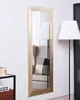 A tall, rectangular gold mirror hangs on a white wall next to a chair and a floor lamp. Náhľad obrázku produktu