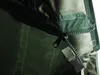 A close-up view of a zipper and buckle on a green fabric item. Voir les images du produit