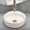 A white ceramic basin with a gold faucet is shown in a bathroom setting with a concrete wall and countertop. Náhľad obrázku produktu