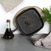 A cast iron grill pan is shown on a wooden board, next to a bottle of olive oil and a folded cloth. Náhľad obrázku produktu