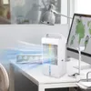 A white portable air cooler is shown on a desk next to a computer monitor displaying a world map. The air cooler is emitting a blue, wavy stream of air, suggesting its cooling function. A desk lamp is visible in the background, and part of a chair is on th Produktbild-Vorschau