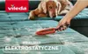 A dog is lying on a teal sofa, and a hand is using a red and black brush to remove pet hair from the sofa. The Vileda logo is in the top left corner. Podgląd zdjęcia produktu