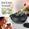 A woman is holding a tea cup, and a hand is adding tea leaves to a teapot. Produktbild-Vorschau