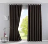 A pair of brown blackout curtains are shown, with one curtain partially drawn back to reveal a window with a green tree and blue sky outside. A small side table with decorative items is visible to the left. Produktbild-Vorschau
