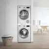A stacked washing machine and dryer unit in a laundry room, with a basket of folded laundry to the left and a dining area in the background. Produktbild-Vorschau