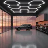 A modern garage or workshop with a car parked inside, illuminated by hexagonal ceiling lights. Podgląd zdjęcia produktu