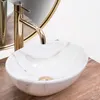 A close-up view of a marble-patterned vessel sink with a gold faucet, placed on a wooden surface. Náhled obrázku produktu