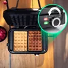 A waffle maker with two waffles, one lighter and one darker, on a wooden surface. A bowl of raspberries is visible on the left. A close-up of the control panel is highlighted with a green circle. Produktbild-Vorschau